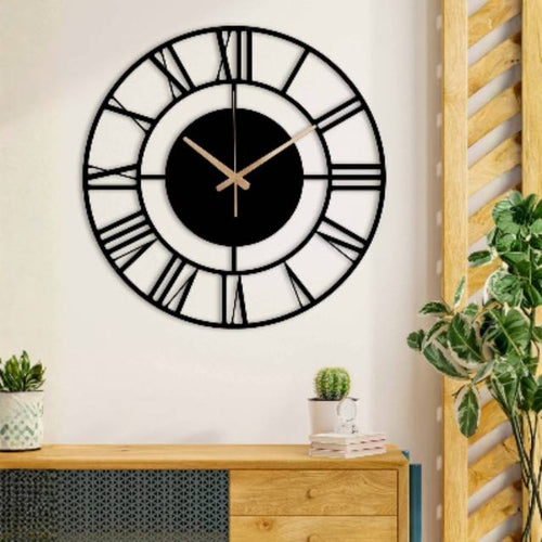 Large wall clock with black face and white numbers on a white wall, with a wooden cabinet and plants in the foreground.