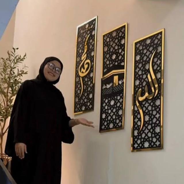 Woman in black attire standing next to three decorative wall panels with Arabic calligraphy.